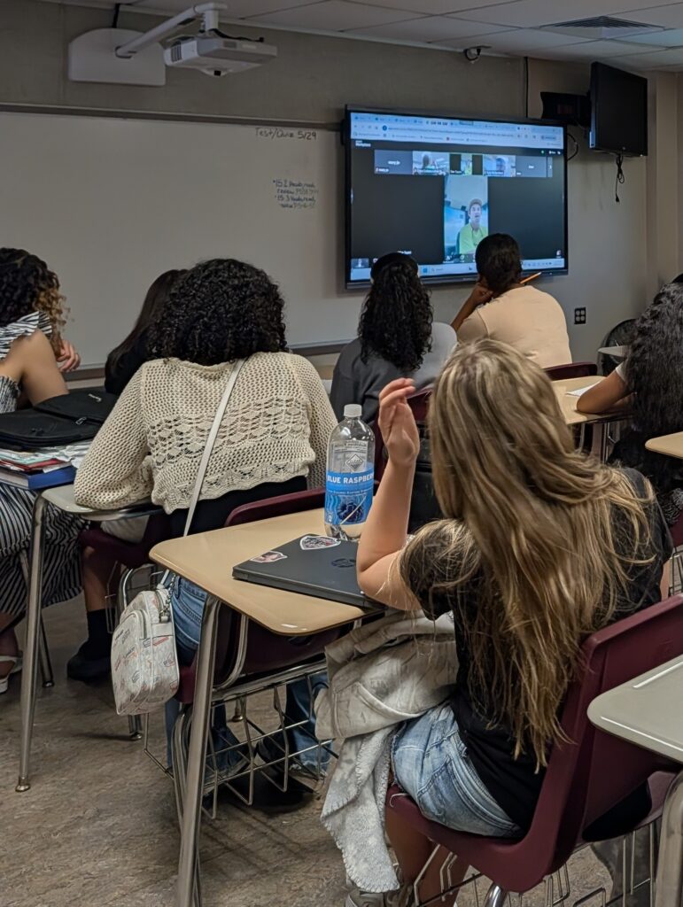 looking on from back of room as students listen to a presenter on screen display.