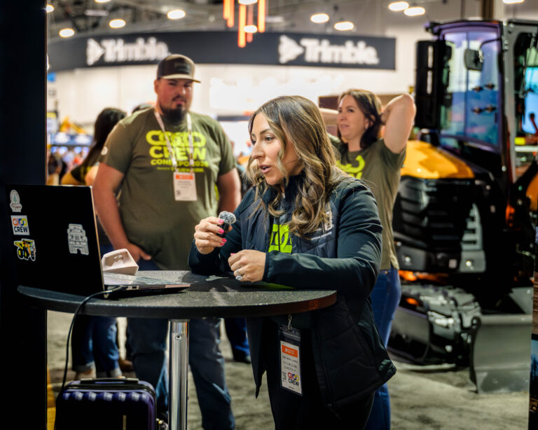 Woman speaking into a microphone with onlookers at an event.